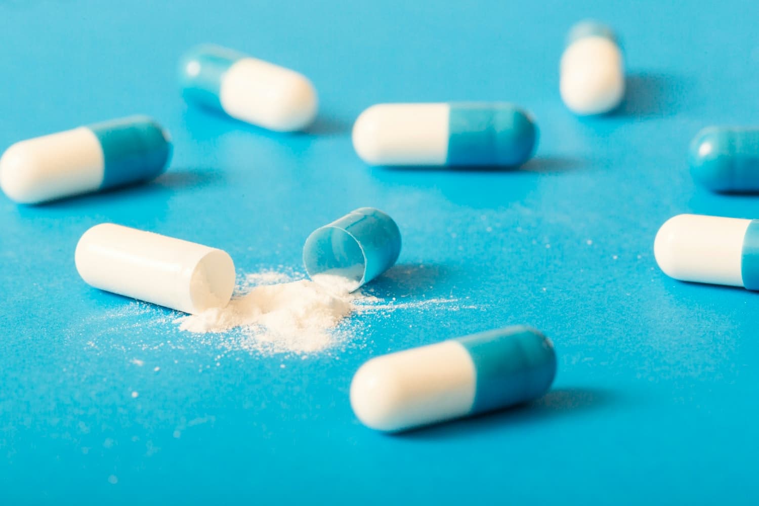 white pharmaceutical powder spilling from broken capsule on blue surface
