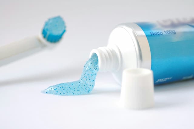 a tube of toothpaste with the paste coming out and the lid unscrewed off.