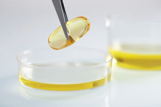 closeup tweezers holding clear yellow capsule yellow liquid glass dish lab
