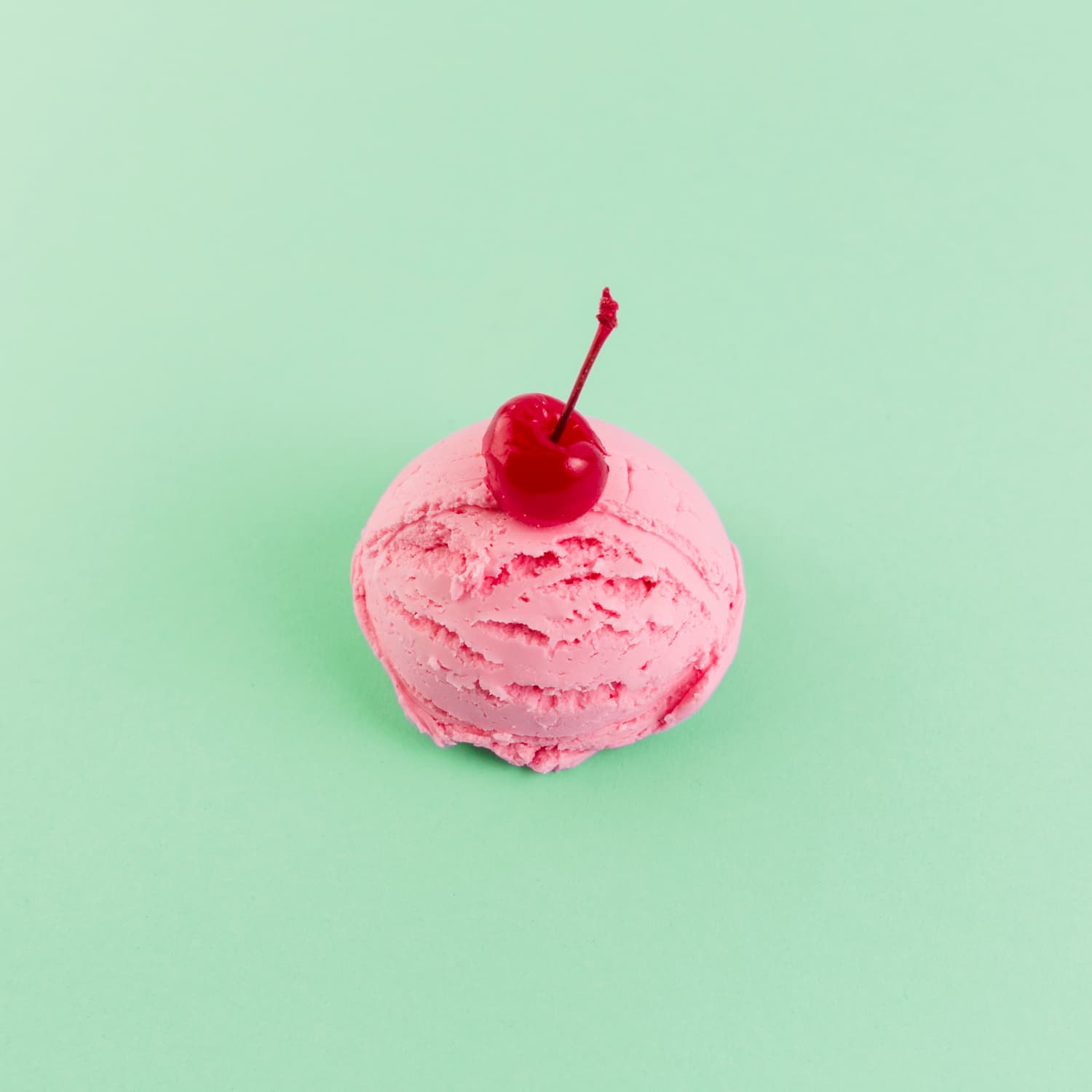 cherry on top of pink-ice-cream against green background