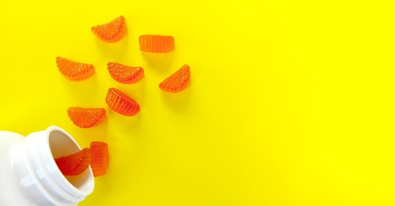 orange-jelly-candies-like-orange-slices-vitamins-scattered-from-jar-isolated-yellow-background