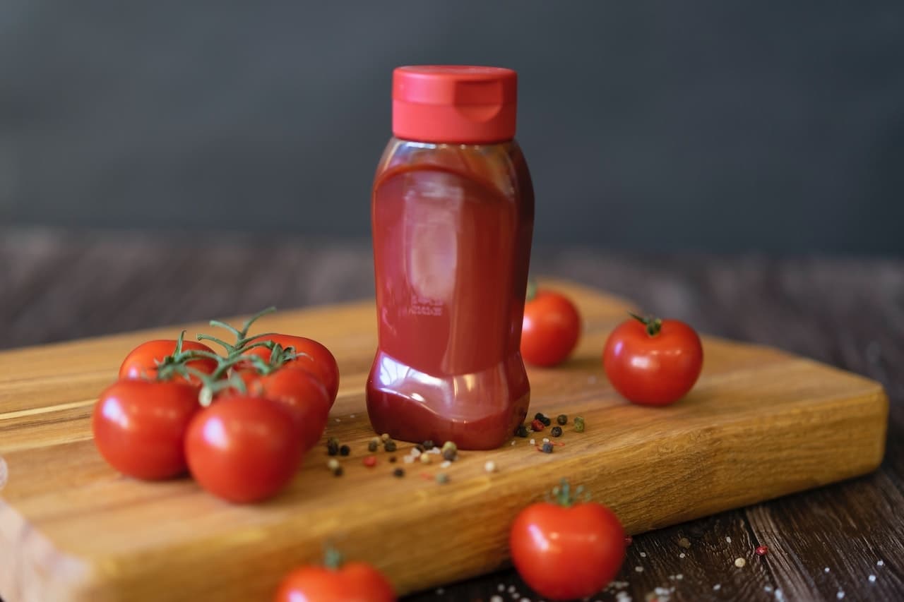 Plastic ketchup bottle on chopping board with tomatoes in background