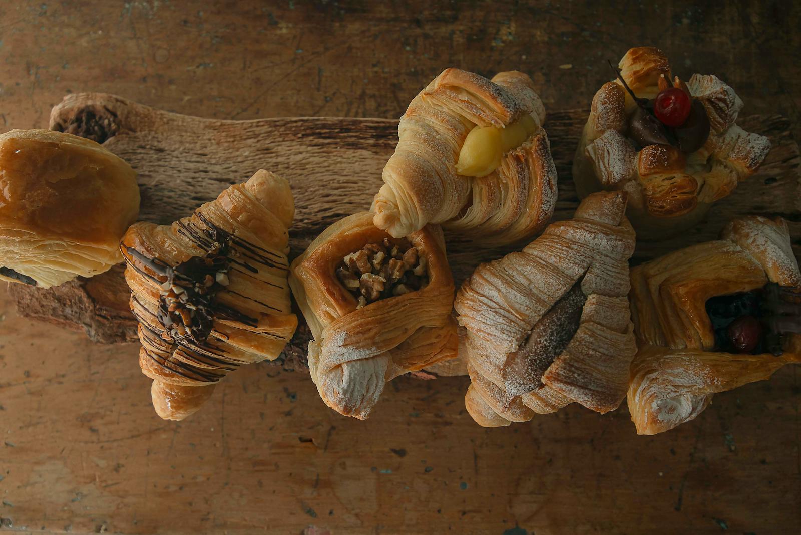A variety of pastries, including croissants and sweet rolls, on a rustic wooden board.