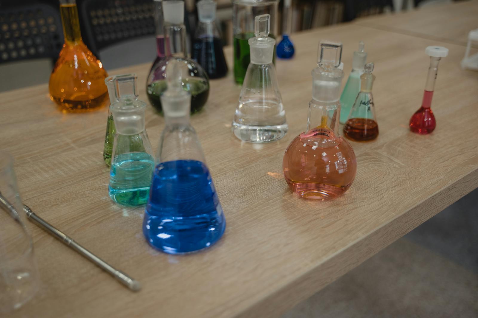 Colorful laboratory flasks with various liquids on a wooden desk for science experiments.
