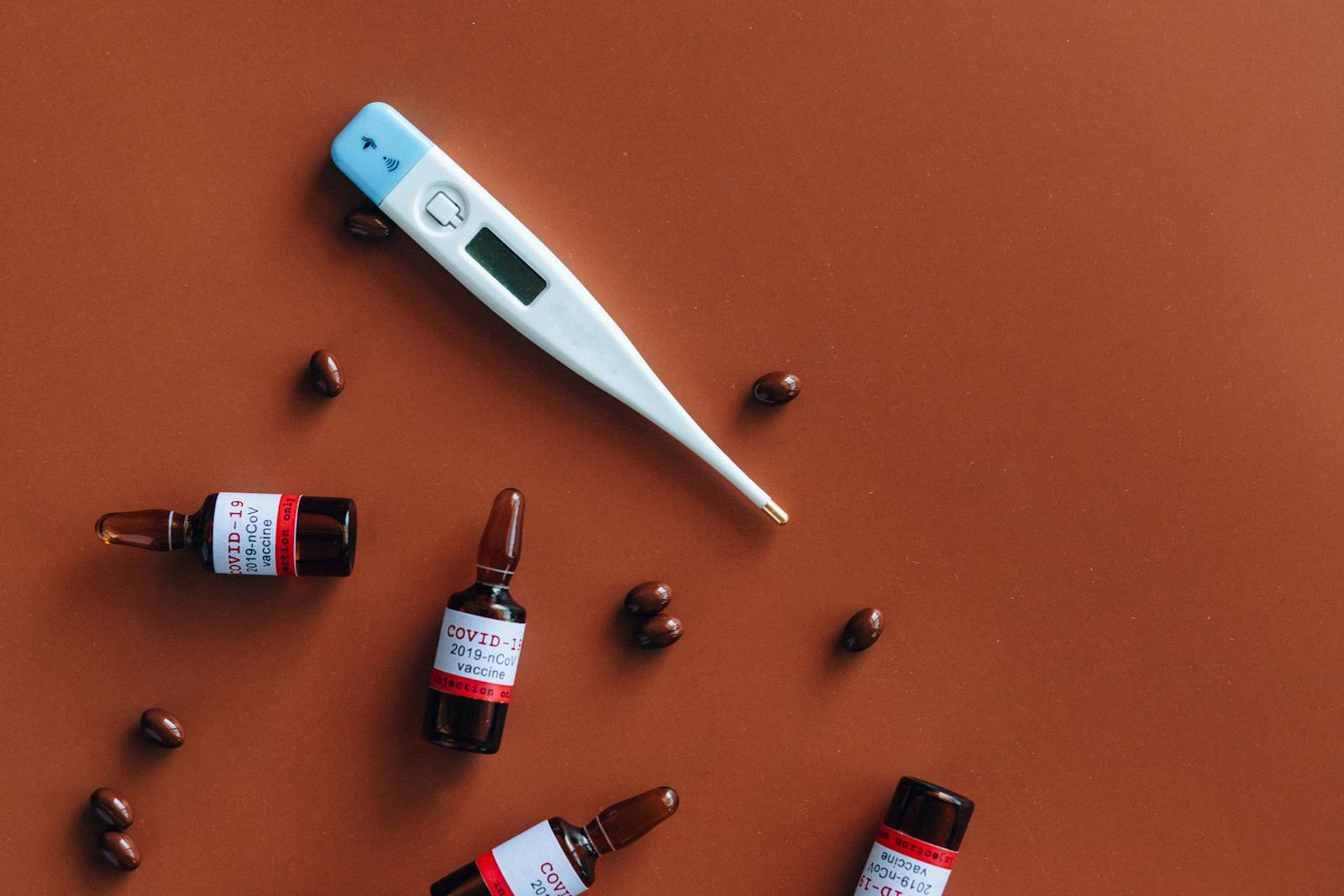 Close-up of COVID-19 vaccine vials, thermometer, and pills on a red background