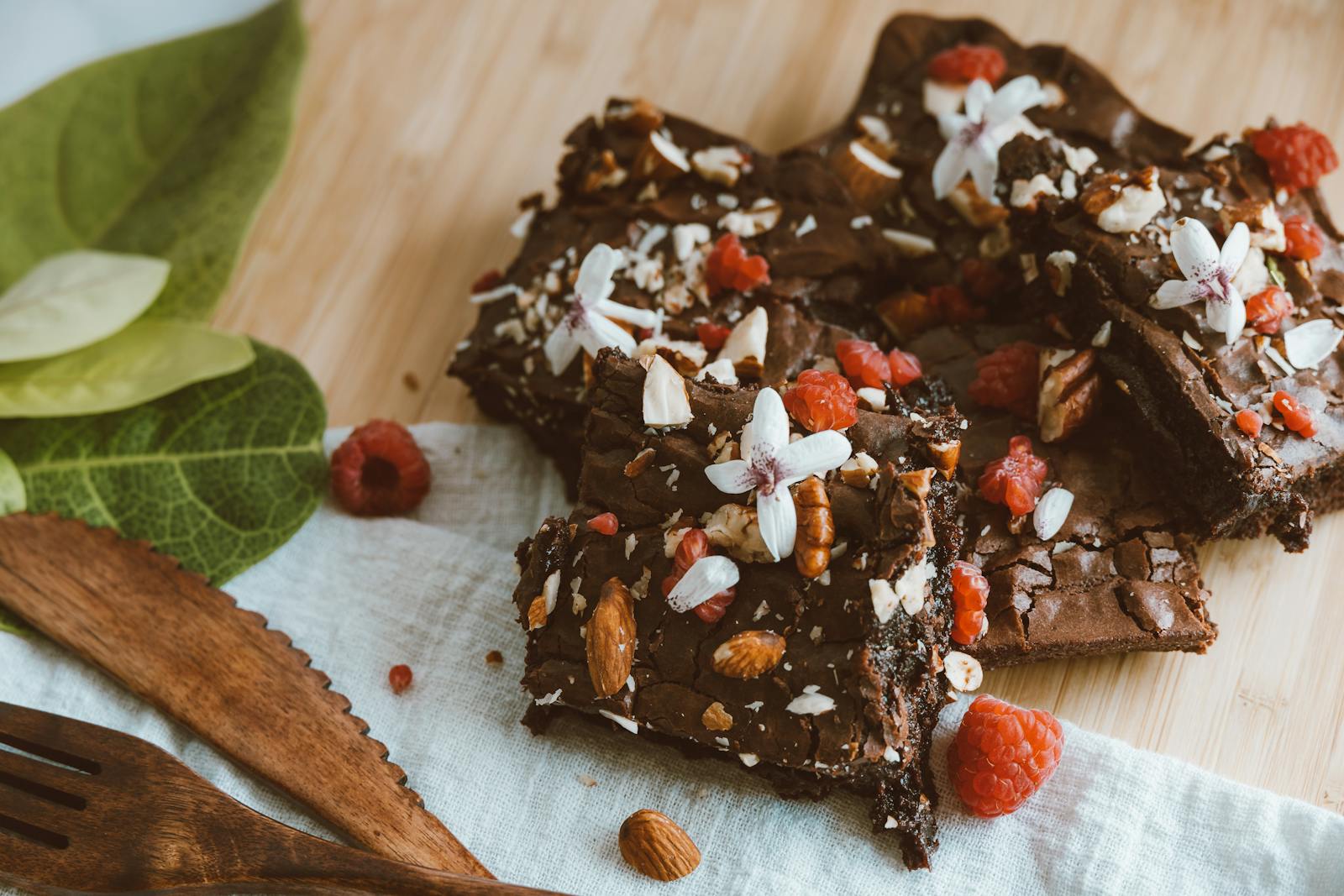 Rich chocolate brownies topped with raspberries, nuts, and flowers on a wooden table.