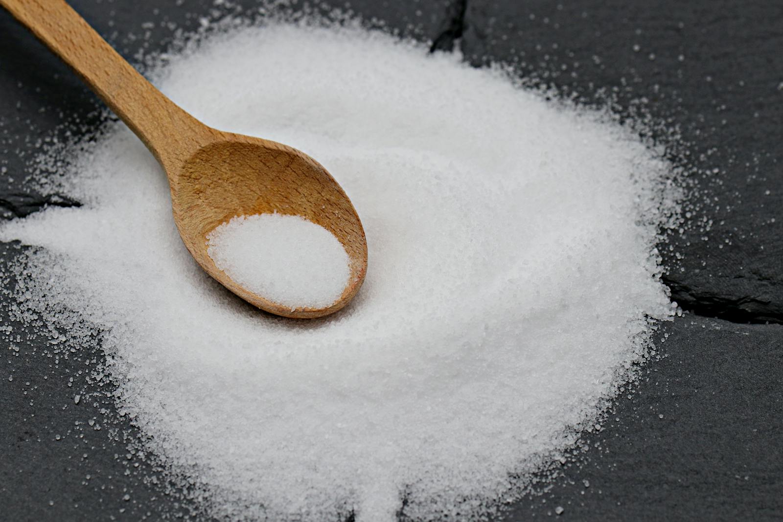 Close-up of a wooden spoon with sea salt on a slate background, perfect for culinary themes.