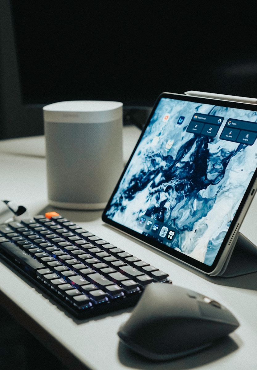 black ipad beside black computer keyboard on white table